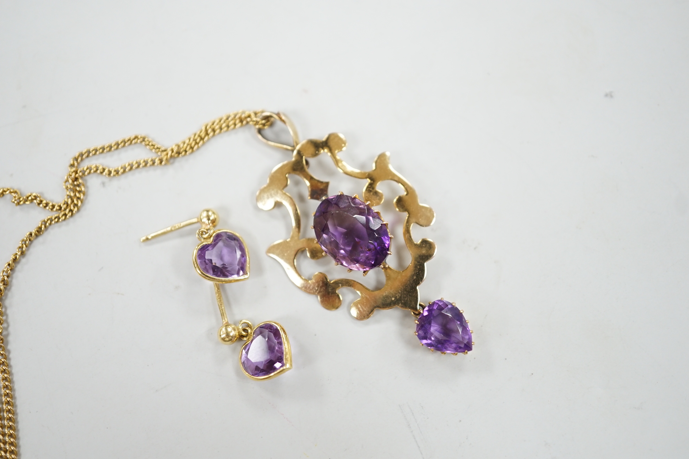 An early 20th century 9ct and two stone amethyst set drop pendant, 40mm, on a 9k chain, 60cm, gross weight 6.8 grams, together with a pair of 18ct gold and heart shaped amethyst set drop earrings, gross 1.6 grams.